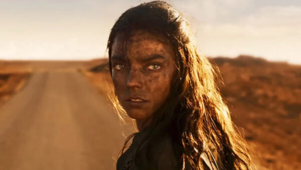 A close-up of Furiosa (Anya Taylor-Joy)'s dirty face in front of a highway