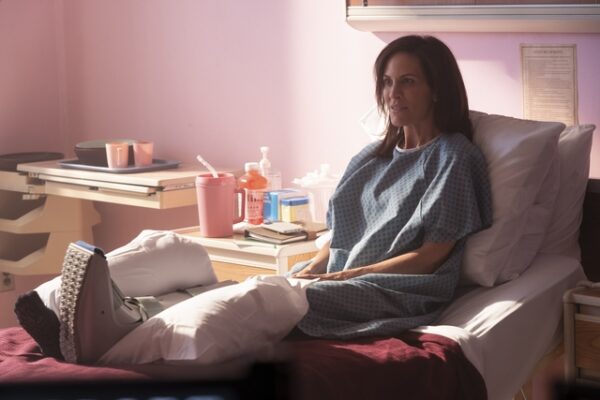 Dr. Sullivan (Annabeth Gish) sits in bed with her left leg in a cast