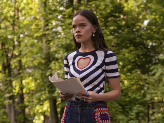 Mouse (malia-pyles) wearing a black and white shirt with heart cut-out, holds a pile of papers in the woods