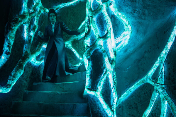 Agatha Harkness (Kathryn Hahn) stands on a flight of blue-lit stairs made out of roots