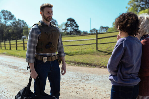 Olsen (Bill Heck) stands with a bag and a badge on a dirt road