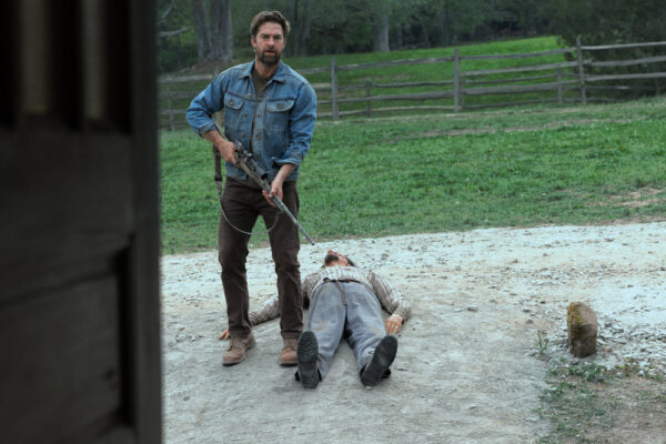 James Chenoweth (Scott Speedman) holding a gun next to the dead body of a man on the ground