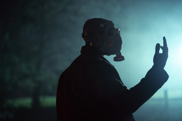 McNab (Rob Morgan) looks at his hand wearing a gas mask