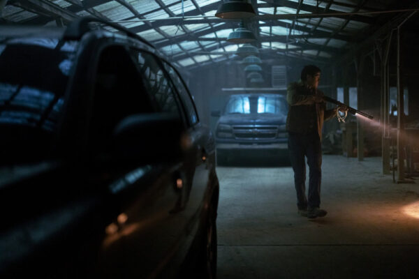 Ruben (Chaske Spencer), holding a gun, searches a garage with cars parked in the foreground and background