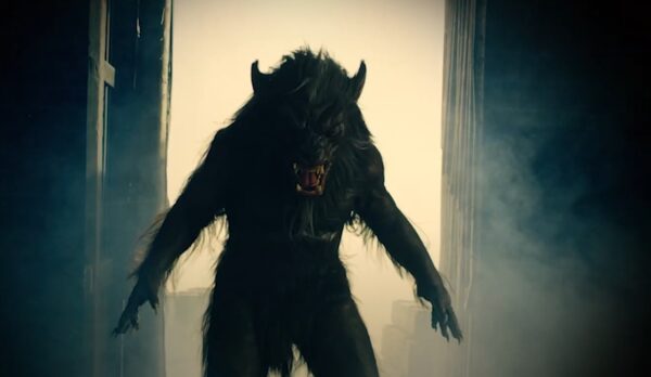 A 3/4 shot of a werewolf standing in a lit doorway with its arms spread at its side