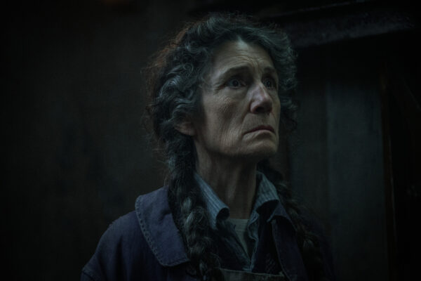 An older white woman with black/grey hair in braids, wearing a blue shirt