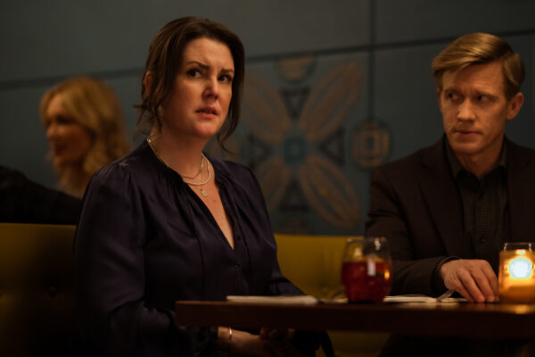 A dark haired middle age woman in a black dress sits at a table in a restaurant