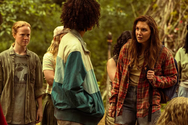 A brunette teen girl looks incredulous at a Black teen girl facing away from the camera in the woods