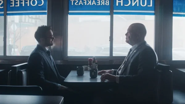 Two men sits across a table at a well lit diner