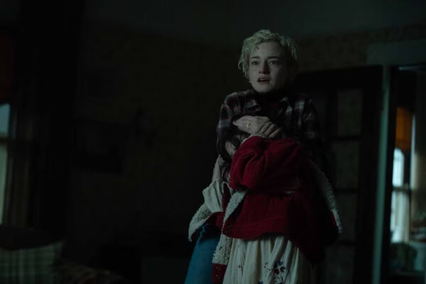 A blonde woman hugs a young dark haired girl in a red coat in the dark