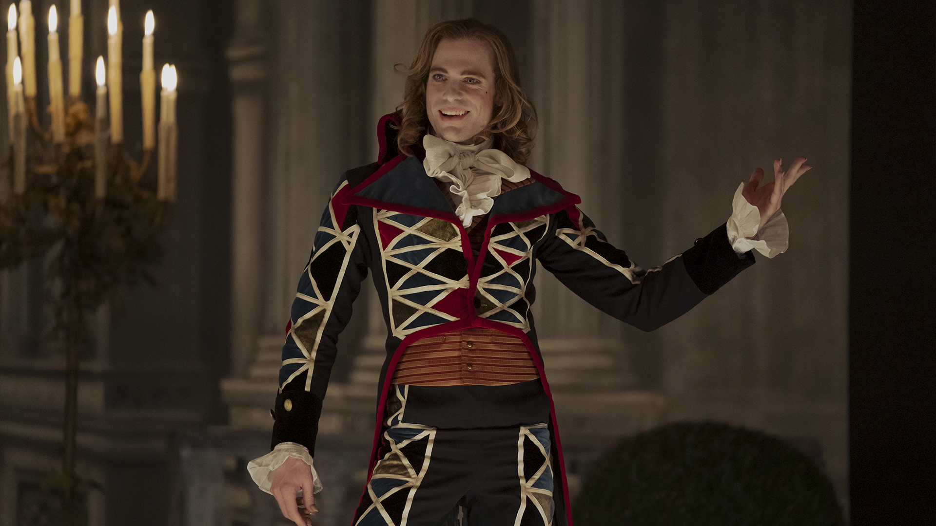 <b>Lestat</b> (Sam Reid) grins on stage in a red and blue stitched outfit.